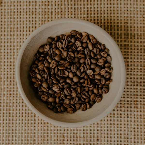 Roasted coffee beans fill a small, rustic bowl