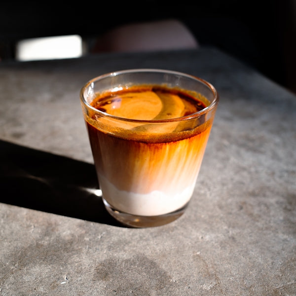 A glass of coffee with cream and sunlight.