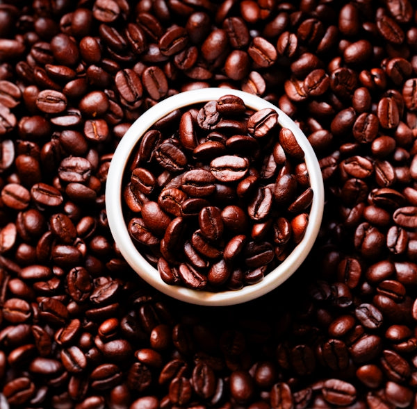 A bowl of roasted coffee beans surrounded by more beans