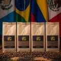 Four coffee bags with a label in front of three flags on a wooden surface.